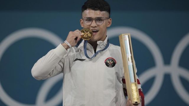 Atlet angkat besi putra Indonesia, Rizki Juniansyah, mempersembahkan medali emas yang ia raih di kelas 73 kg putra Olimpiade Paris 2024